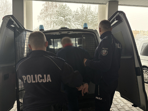 Policjanci prowadzą zatrzymanego do radiowozu.