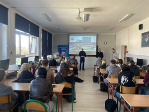 Na zdjęciu widoczni od strony lewej I Zastępca Komendanta Powiatowego Policji w Olkuszu, obok stoi Zastępca Naczelnika Wydziału Prewencji. W tle prezentacja multimedialna.