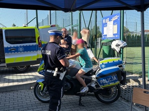 Policjant z uczestnikami wydarzenia przy motocyklu.