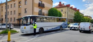 Policjant ruchu drogowego przekazuje ulotki kierowcy autobusu szkolnego informując o nowych przepisach. W tle bloki i samochody na osiedlowych parkingach oraz ulice.