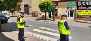 Policjantka i policjant ruchu drogowego w odblaskowych kamizelkach stoją przy przejściu dla pieszych trzymając ulotki informujące o nowych przepisach.