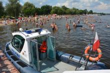 Policyjna łódź na wodzie. W tle plaża i wypoczywający ludzie.