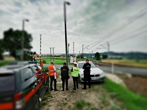 Policjantka, pracownik PKP oraz dwóch funkcjonariuszy Służby Ochrony Kolei przy przejeździe kolejowym. w tle pojazd SOK oraz nieoznakowany radiowóz policyjny.
