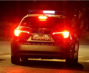 Radiowóz w porze nocnej - widok z tyłu samochodu. Widać podświetlony napis policja na dachu radiowozu oraz na tylnej klapie numer rejestracyjny &quot;HPGC090&quot;. Samochód jest w ruchu , święcące się światła hamowania.