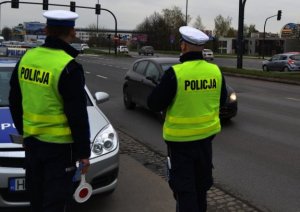 Policjanci ruchu drogowego stoją przy radiowozie i obserwują poruszające się po drodze pojazdy.