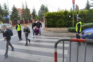 Przejście dla pieszych po którym przechodzą dorośli i dzieci. obok stoi policjantka ruchu drogowego i zatrzymuje ruch na drodze.