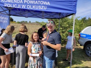 Mężczyzna w alkogoglach przy stanowisku policyjnym. Obok stanowiska gromadzą się dzieci.