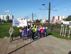 Policjant z dziećmi podczas akcji profilaktycznej. Dzieci trzymają w ręce transparent.