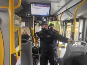 Dwaj policjanci w autobusie legitymują osobę, która nie stosuje się do obowiązku zasłaniania ust i nosa.