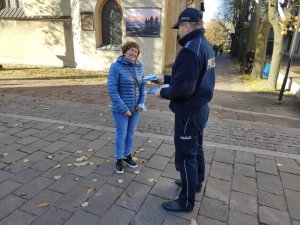 Policjant wręcza ulotkę kobiecie. W tle widać część budynku.