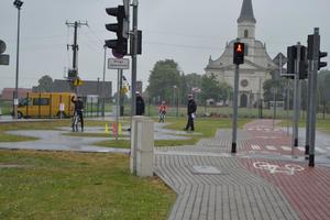 Miasteczko ruchu drogowego, alejki ze znakami i sygnałami świetlnymi. W tle widać policjant ruchu drogowego. Pogoda pochmurna, deszczowa.