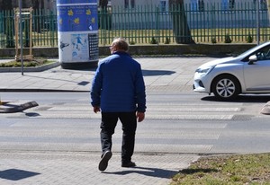 Pieszy wchodzi na przejście dla pieszych. W tle widać samochód, który zatrzymał się przed przejściem. Pogoda słoneczna.