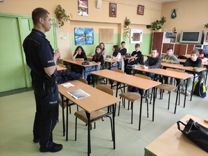 Dzielnicowy rozmawia z uczniami o cyberzagrożeniach. Zajęcia odbywają się w klasie, dzieci siedzą w szkolnych ławkach.