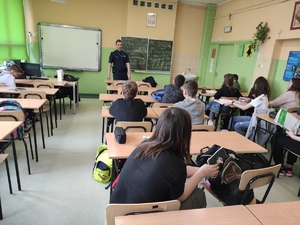 Policjant w klasie rozmawia z uczniami, którzy siedzą w szkolnych ławkach.