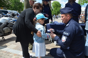 Policjant daje dziewczynce naklejkę z Inspektorem Wawelkiem (policyjna maskotką).