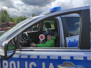 2.	Dziecko w policyjnej czapce trzyma w ręce  tarcze stop, siedzi za kierownicą radiowozu.