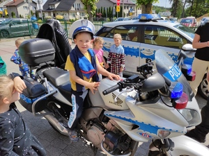 Przedszkolak w czapce policjanta ruchu drogowego na motocyklu. W tle radiowóz policyjny.