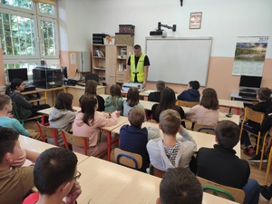 Technik kryminalistyki na spotkaniu z uczniami w klasie prowadzi zajęcia. Dzieci siedzą w szkolnych ławkach.