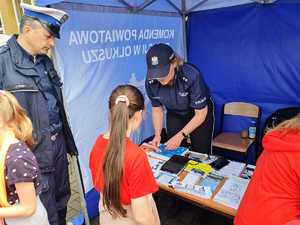 Policjantka wykonuje dzieciom odciski palców. Przy namiocie stoi policjant Wydziału Ruchu Drogowego (biała czapka).