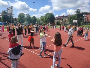 Rozbawione dzieci tańczą na boisku szkolnym. Pogoda słoneczna.