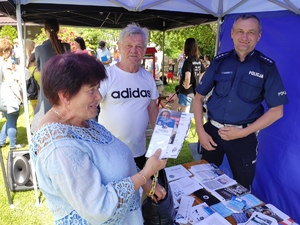 Policjant ruchu drogowego przy stanowisku policyjnym rozmawia z kobieta i mężczyzną. Kobieta w ręku trzyma ulotki.