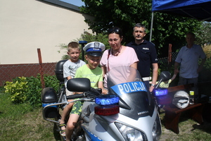 Dwóch chłopców siedzi na motocyklu policyjnym, obok stoi kobieta, za nimi policjant ruchu drogowego.