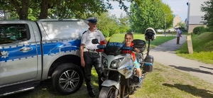 Przy policyjnym radiowozie na motocyklu siedzący chłopczyk i obok stojący policjant z Ruchu Drogowego