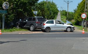 Dwa samochody osobowe seat i volkswagen po zderzeniu. Samochody uszkodzone (przód seata,podniesiona, wygięta  maska). W tle  droga, wzdłuż niej drzewa i słupy wysokiego napięcia. Pogoda letnia.bezchmurne niebo.