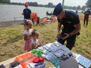 Dwie dziewczynki przy stanowisku policyjnym. Policjant wykonuje dzieciom odbitki linii papilarnych.