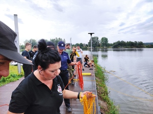 Strażacy rzucają rzutki do wody. W tle policjantka ściąga z wody  rzutkę.