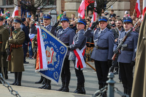 Poczet sztandarowy składający się z policjantów kompanii honorowej w mundurach galowych podczas odchodów Święta Niepodległości. Policjant trzyma opuszczony sztandar na znak &quot;baczność&quot;