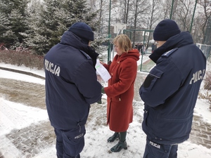 Dyrektor Zespołu Szkół nr 1 w Olkuszu przekazuje policjantom dokumenty. W tle,  na placu stoi grupa ewakuowanej młodzieży  szkolnej