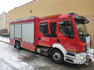 Wóz strażacki na sygnałach w gotowości zaparkowany na terenie szkoły.