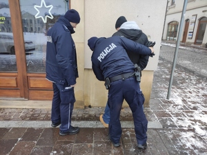 Dzielnicowi zatrzymali pozoranta przed jednym ze sklepów w Olkuszu. Dzielnicowy przeszukuje zatrzymanego. Drugi z policjantów, asekuruje mu w tej czynności