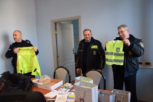 Policjant i funkcjonariusz trzymają w ręce kamizelki odblaskowe. Zdjęcie wykonane w pomieszczeniu budynku Komisariatu Policji w Wolbromiu.