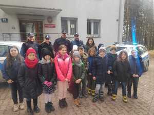 Grupa trzecioklasistów wraz z policjantami stoją przed budynkiem Komisariatu Policji w Bukownie. Za uczniami po prawej i lewej stronie radiowozy.