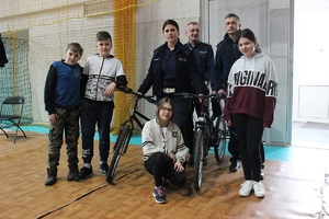 Dwóch policjantów i policjantka w towarzystwie czterech uczestników turnieju stoją przy rowerach, na których uczniowie pokonywali tor przeszkód.