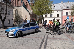 Radiowóz policyjny na trasie rajdu rowerowego, a za nim grupa osób jadących na rowerach