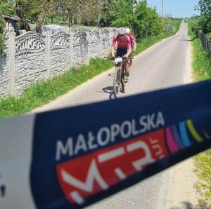 Rowerzysta podczas maratonu. W tle taśma zabezpieczająca i napisy  Małopolskie MTB Tour 2023.
