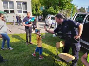 Policjant przybija piątkę dziecku. W oddali widać budynek szkoły i ludzi.