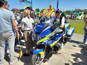 Kobieta w białej czapce policjanta ruchu drogowego na motocyklu. W tle gromadzą się ludzie.