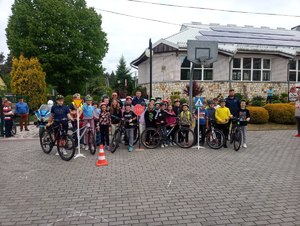 Dzieci z rowerami wśród nich dwaj policjanci. W tle budynek Szkoły Podstawowej w Bydlinie.