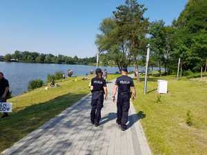 Policjant i policjantka nad zalewem. Przy brzegu wędkarze.