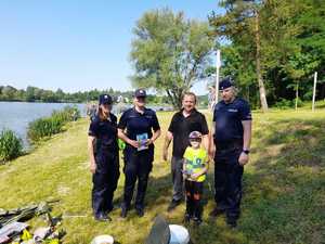 Troje policjantów z mężczyzna i dzieckiem w odblaskowej kamizelce. W tle zalew wolbromski i pejzaż.