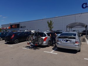 Policjant na parkingu przy centrum handlowym sprawdza czy w zaparkowanym pojeździe nie znajdują się pozostawione osoby lub zwierzęta. Pogoda letnia bezchmurne niebo. W tle budynek, parking i zaparkowane samochody