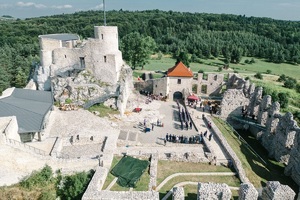 Zdjęcie z drona )(z góry) Ruiny zamku w Rabsztynie na tle pejzażu. Dookoła zamku mury. Po prawej stronie baszta. W środku grupa policjantów i ludzi. Policjanci stoją w równych szykach.