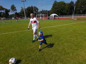 Dziecko wraz z dorosłym na boisku sportowym  biegnie w kierunki piłki