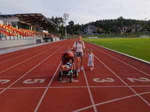 Uczestnicy eventu - kobieta z dwóją dzieci, jedno w wózku stoją na bieżni sportowej.