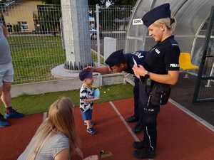 Policjantka oraz policjant pochyla się nad dzieckiem. Policjant głaszcze dziecko po głowie. Obok kuca kobieta.