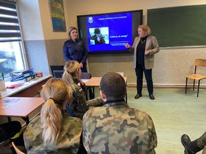 Przodem do zdjęcia policjantka z rektorem uczelni. W ławkach siedzą uczniowie.